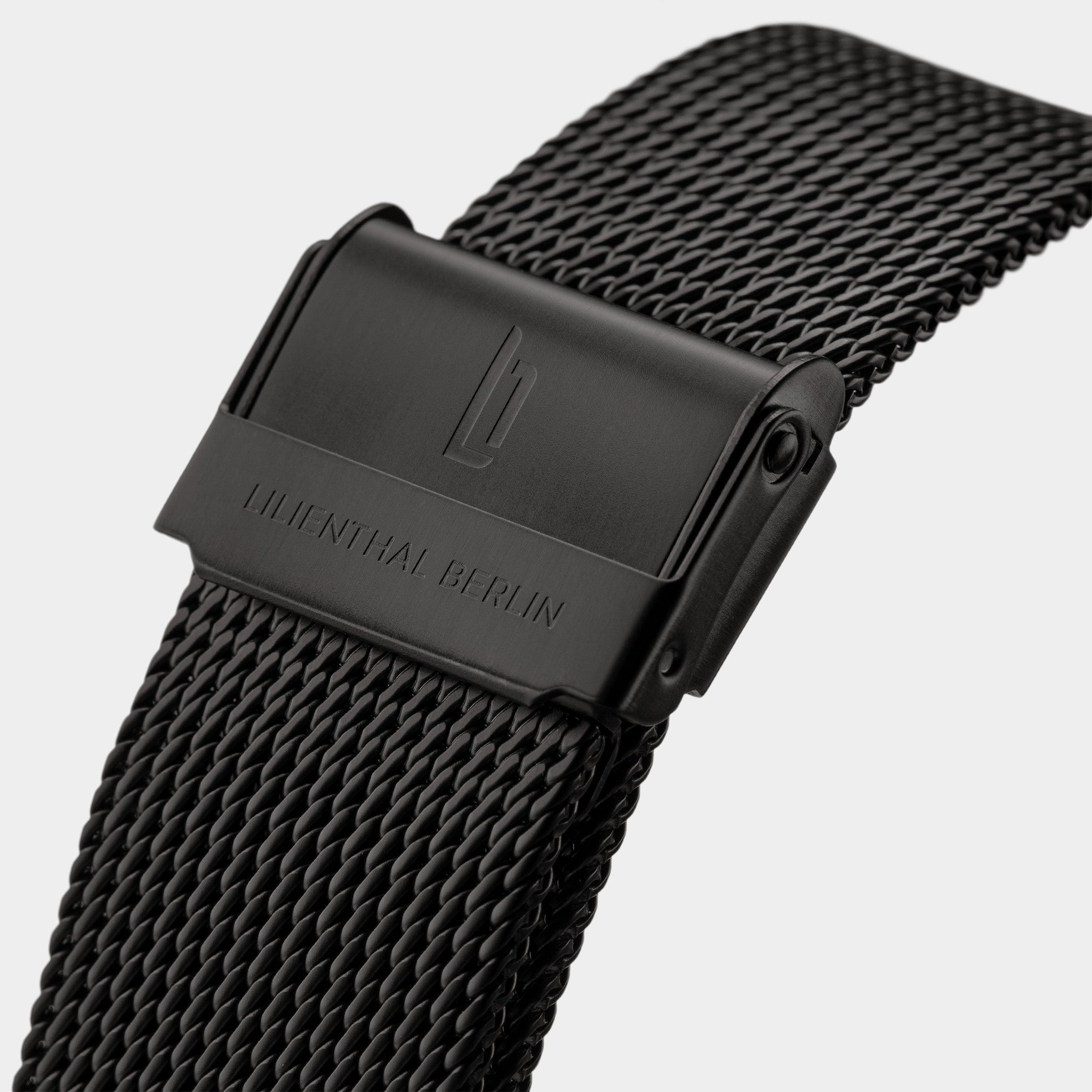 Close-up of black mesh watch strap with engraved clasp and modern textured finish