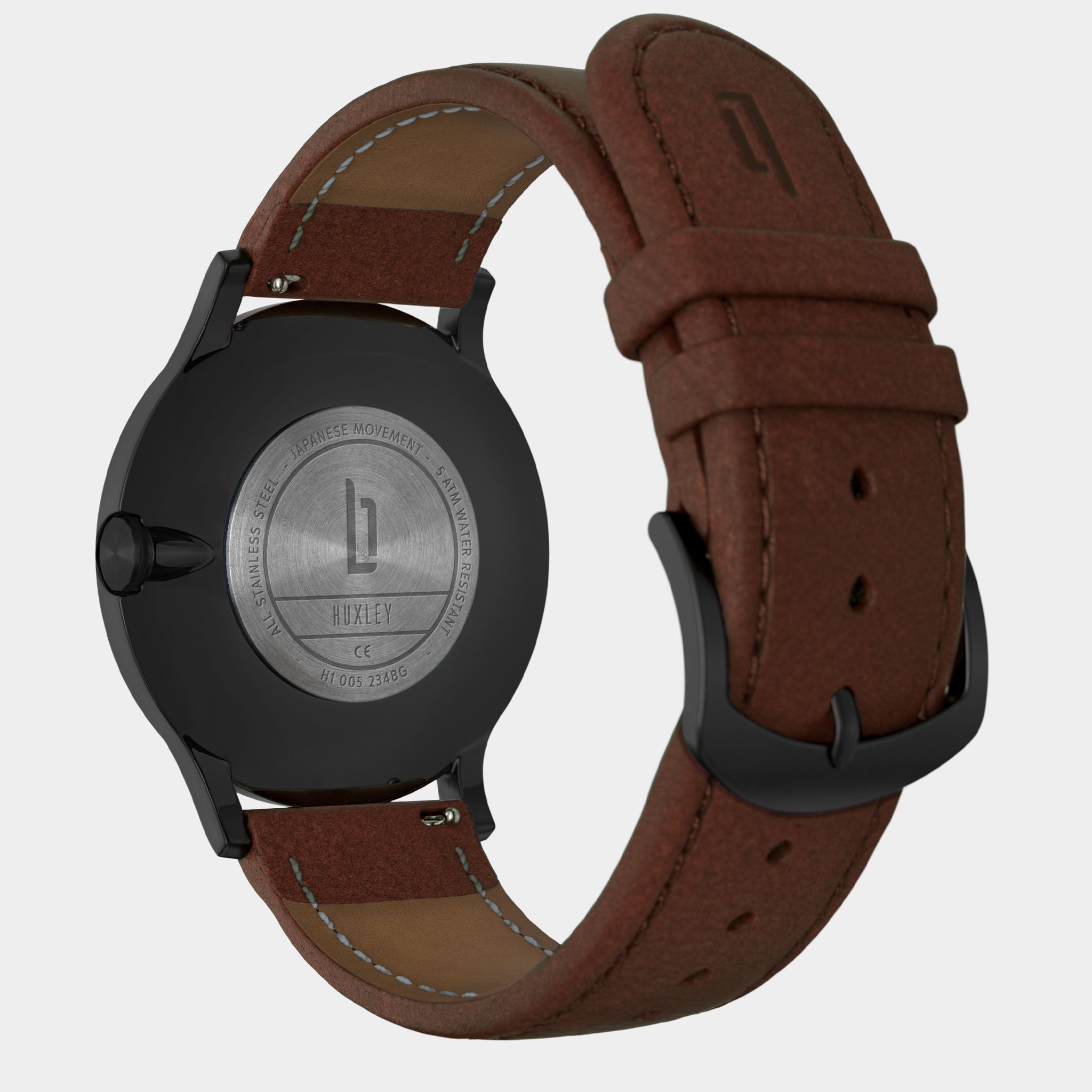 Close-up of the back of a black wristwatch with brown leather strap and engraved caseback.