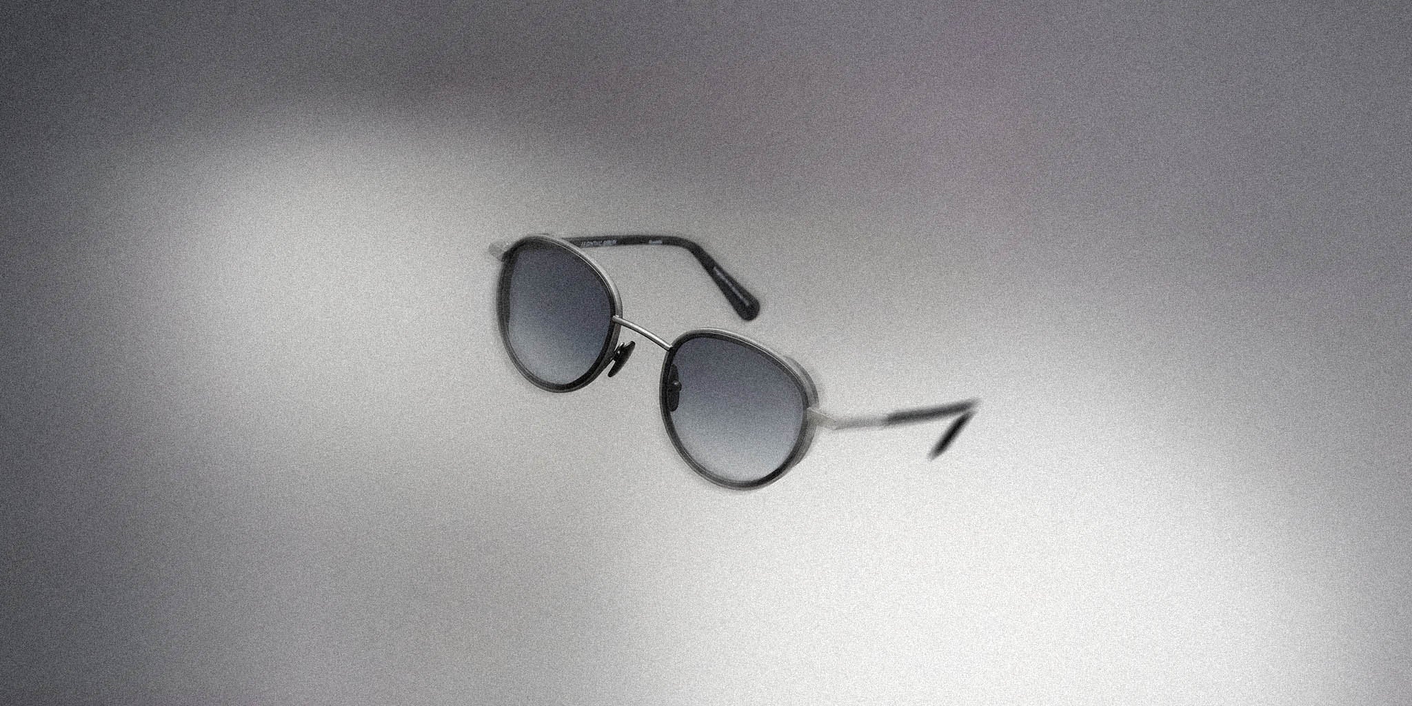 Round sunglasses with black gradient lenses and thin metal frame on a gray background