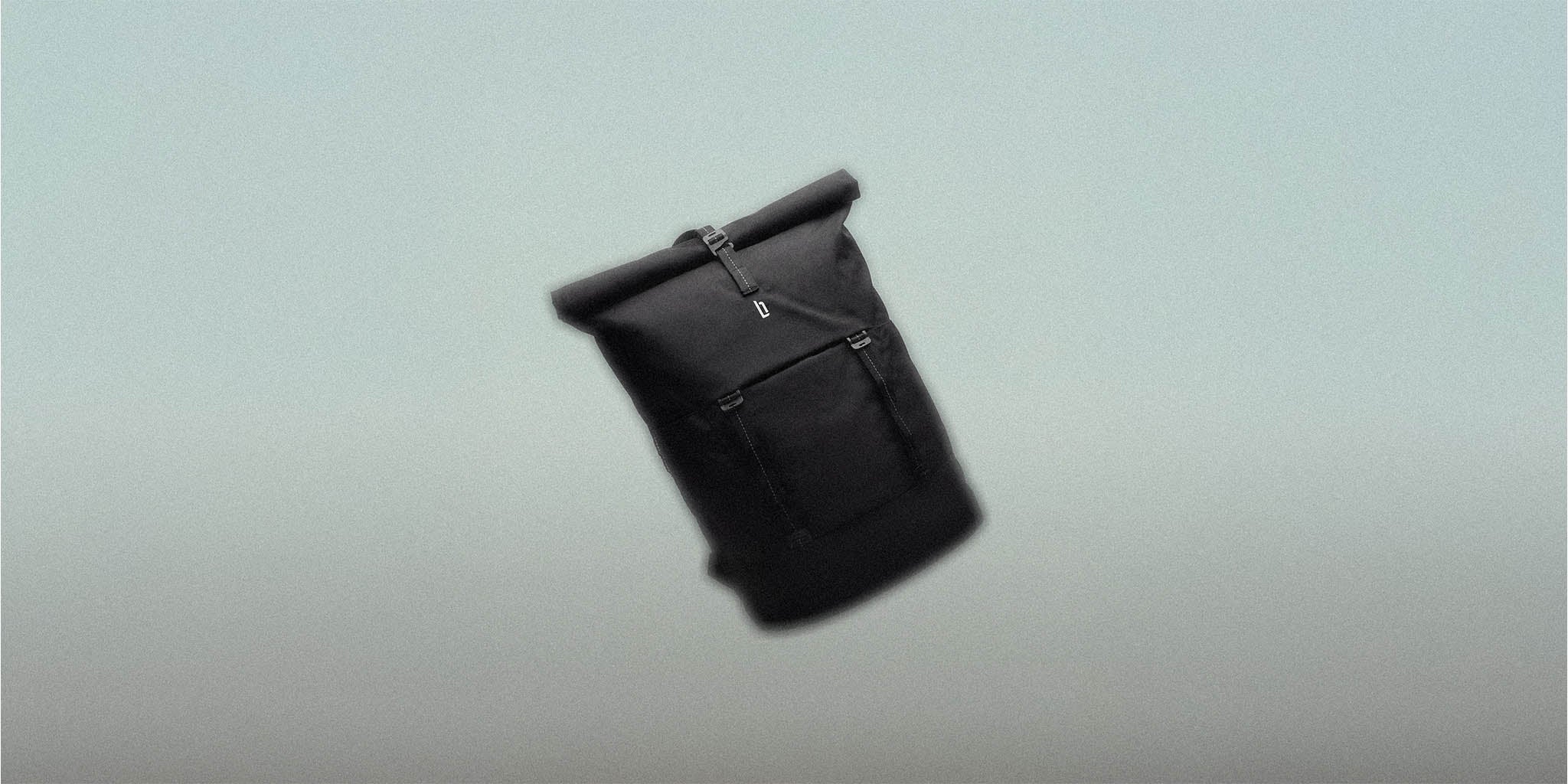 Minimalist black rolltop backpack with front pocket on neutral background