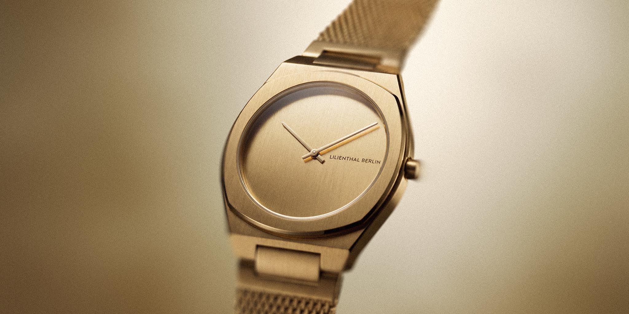 Minimalist gold wristwatch with mesh strap and sleek dial on a neutral background