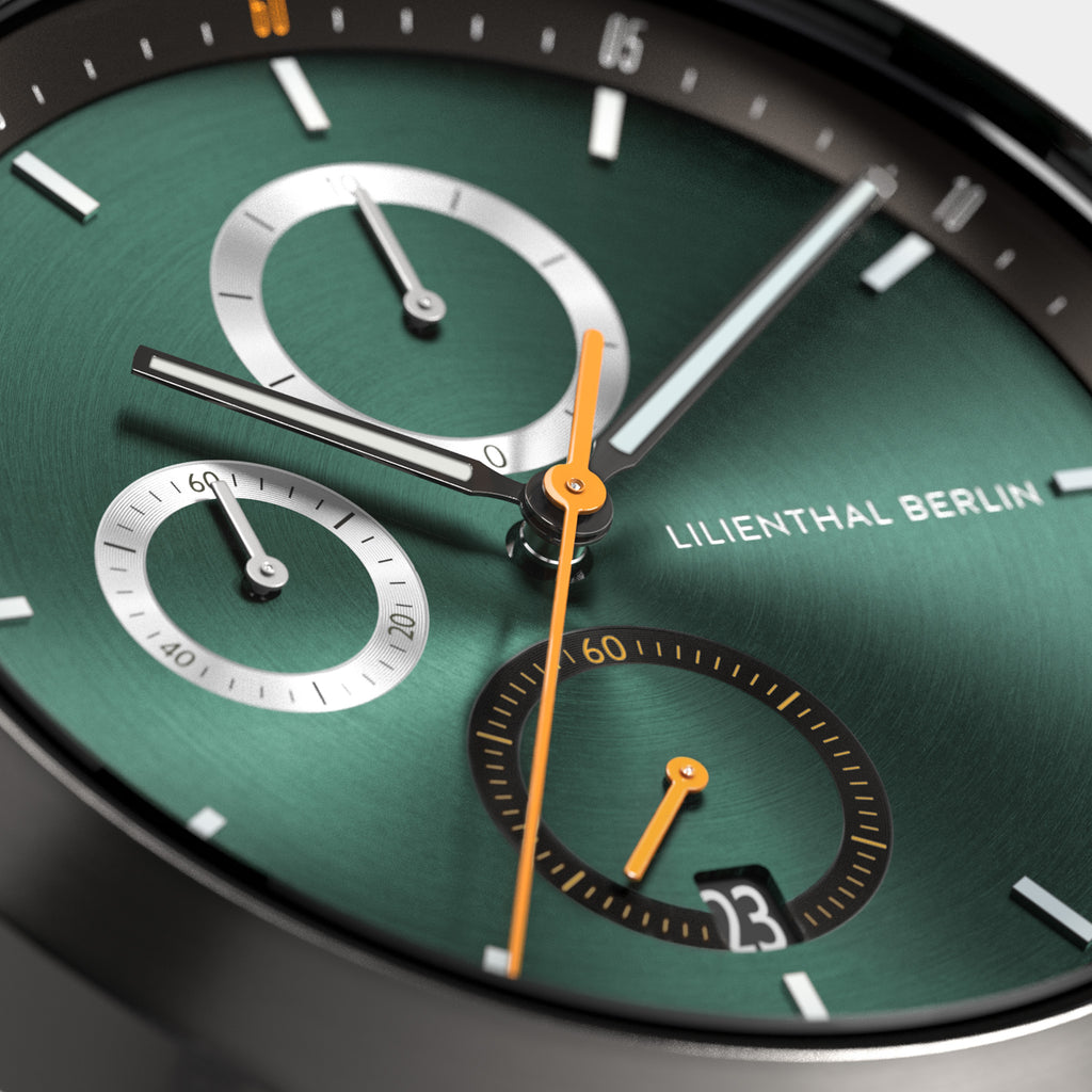 Close-up of a modern green chronograph watch face with orange and silver hands, date display