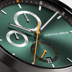 Close-up of a modern green chronograph watch face with orange and silver hands, date display