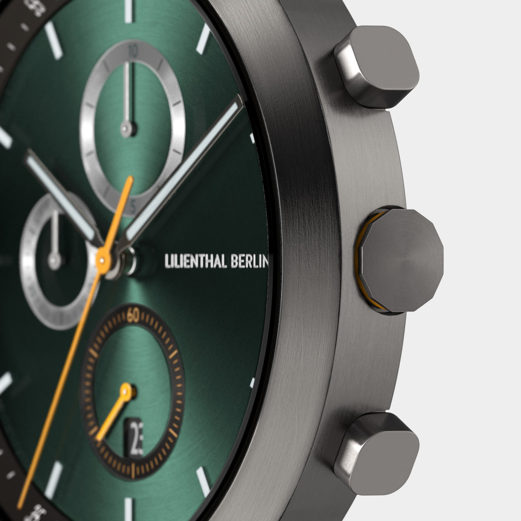 Close-up of a green chronograph watch face with silver dials and push buttons
