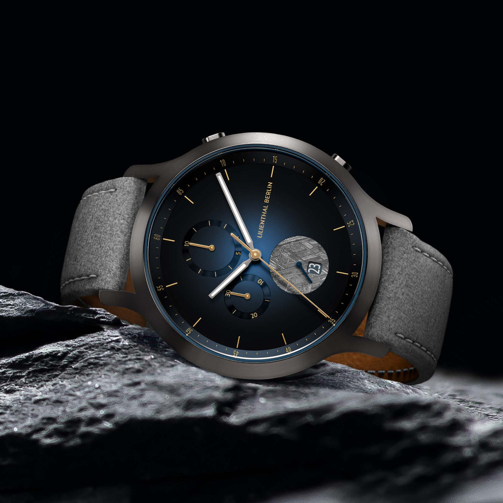Elegant black wristwatch with gold details, blue dial, grey leather strap, date display