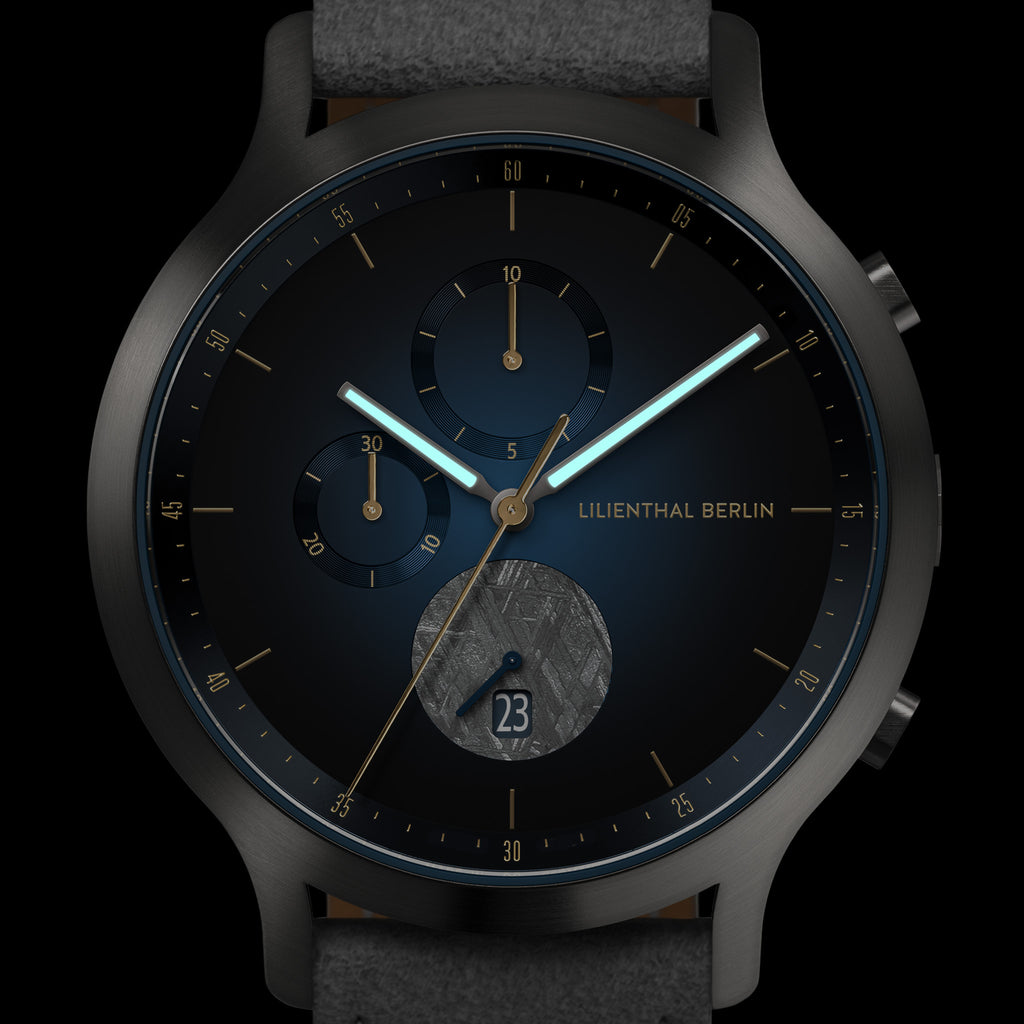 Close-up of a modern black wristwatch with blue details, subdials, date display, and luminous hands