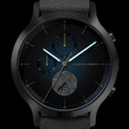Close-up of a modern black wristwatch with blue details, subdials, date display, and luminous hands