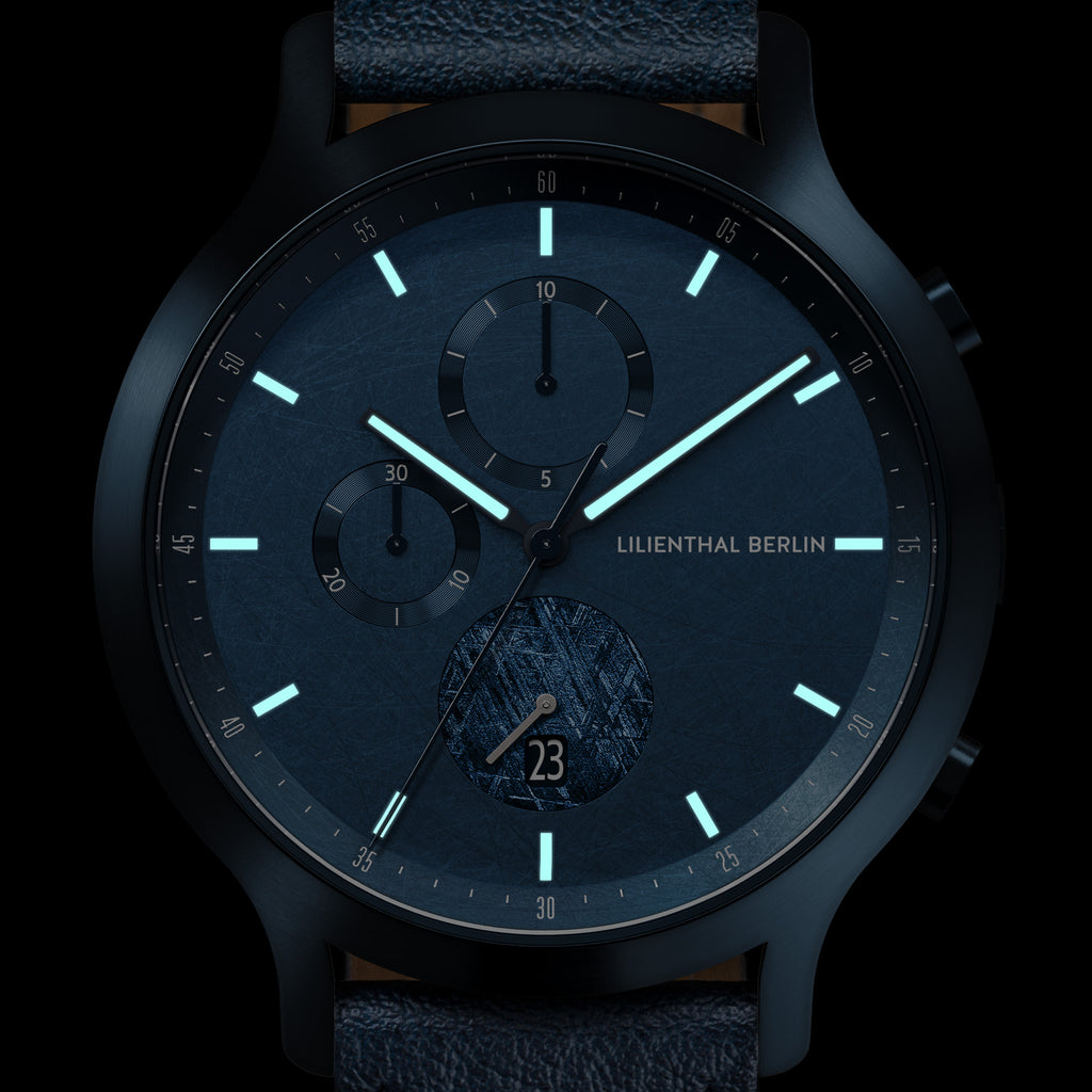 Modern black and blue chronograph watch with luminous hands and subdials on dark background