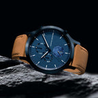 Elegant blue dial wristwatch with tan leather strap on rock, modern minimalist design
