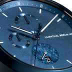 Close-up of a blue chronograph watch face with textured dial, subdials, and date display