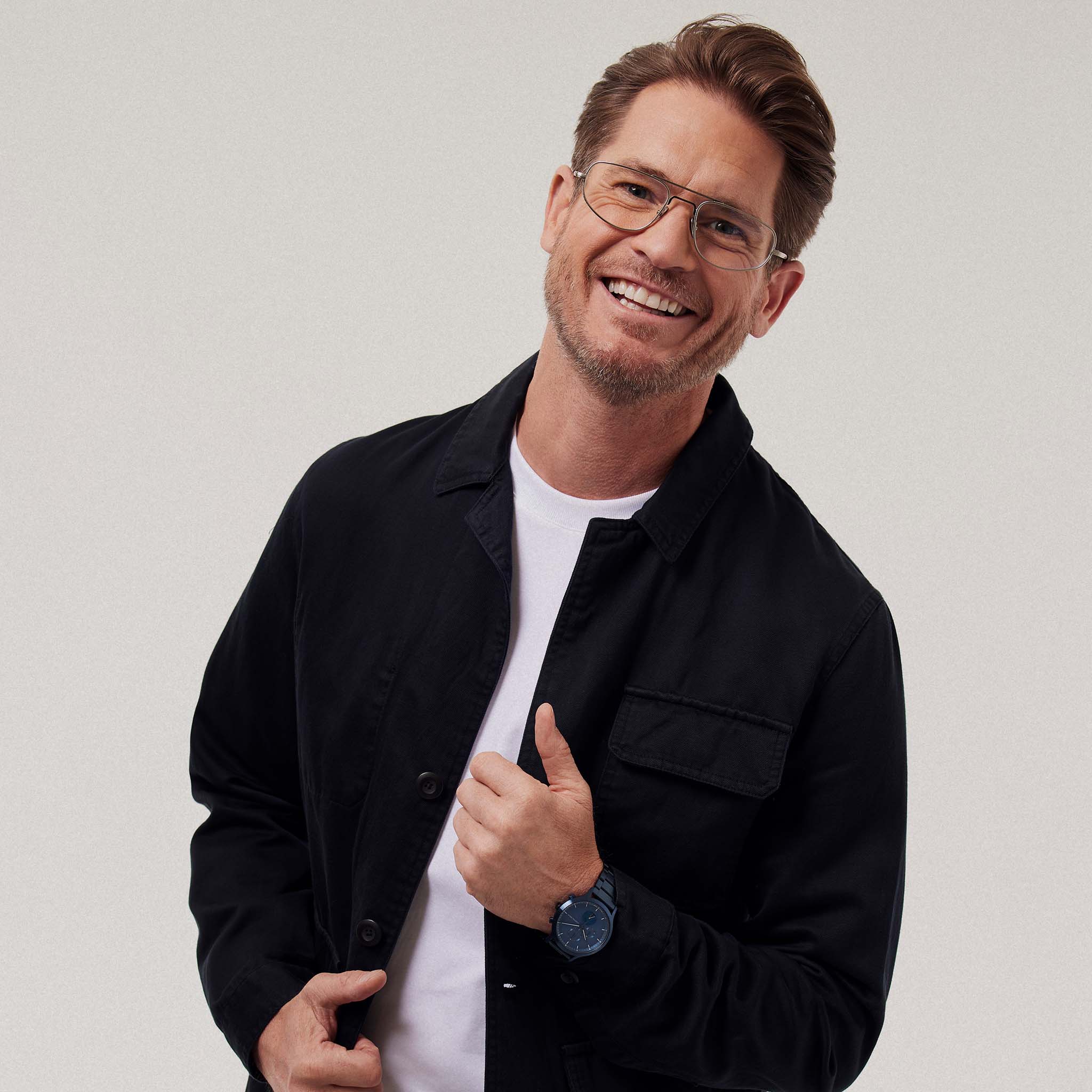 Smiling man wearing glasses, a black jacket, and a modern blue wristwatch.