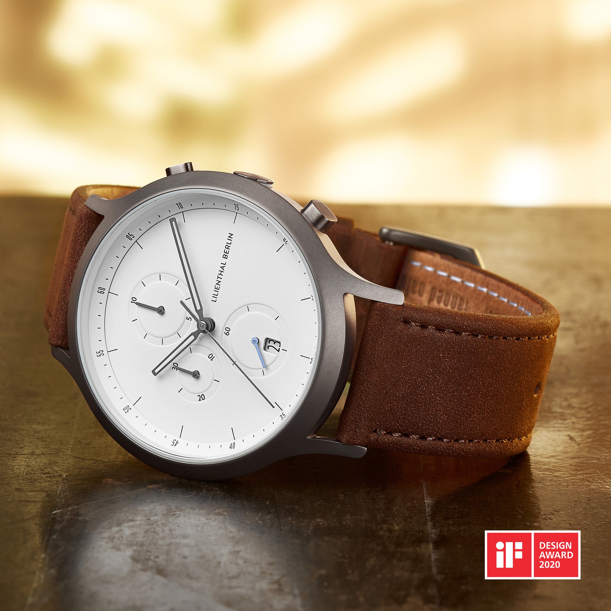 Minimalist silver chronograph watch with white dial and brown leather strap on table