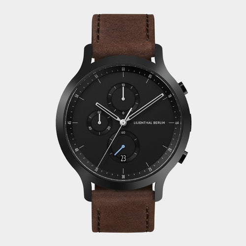 Black chronograph watch with brown leather strap and date display on white background