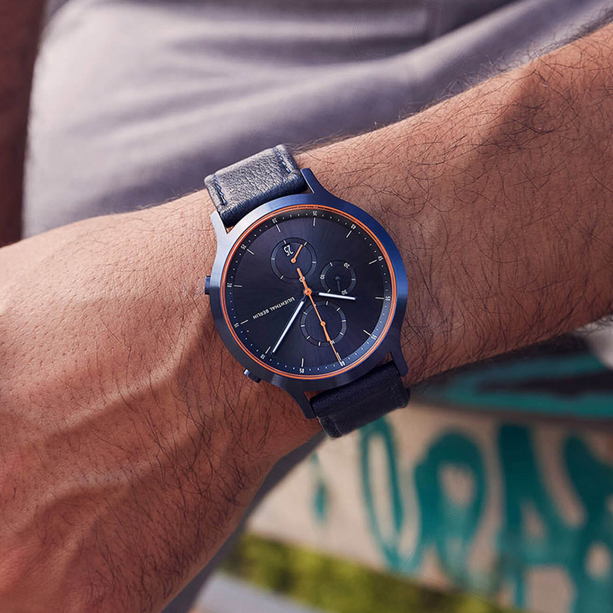 Modern blue chronograph watch with orange accents and leather strap on wrist outdoors