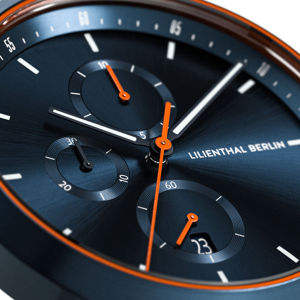Close-up of a modern chronograph watch with blue dial and orange accents, date window visible.