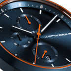 Close-up of a modern chronograph watch with blue dial and orange accents, date window visible.