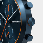 Close-up of modern black chronograph watch with orange accents and textured pushers