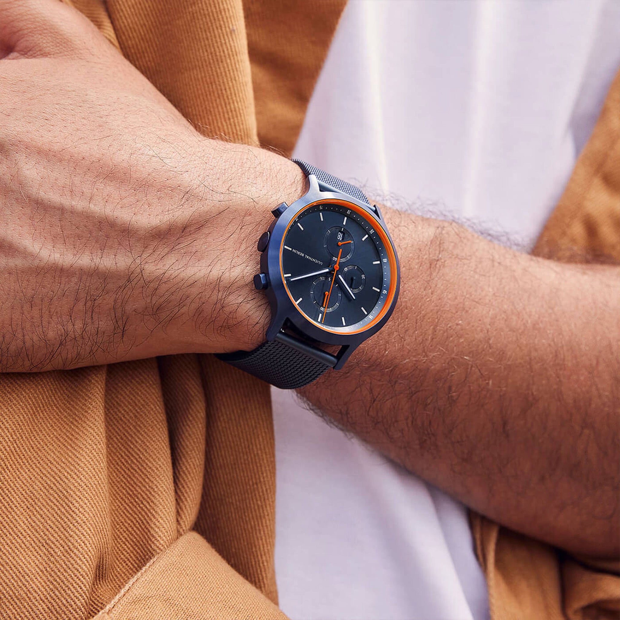 Modern men's chronograph watch with navy mesh strap and orange accents on wrist