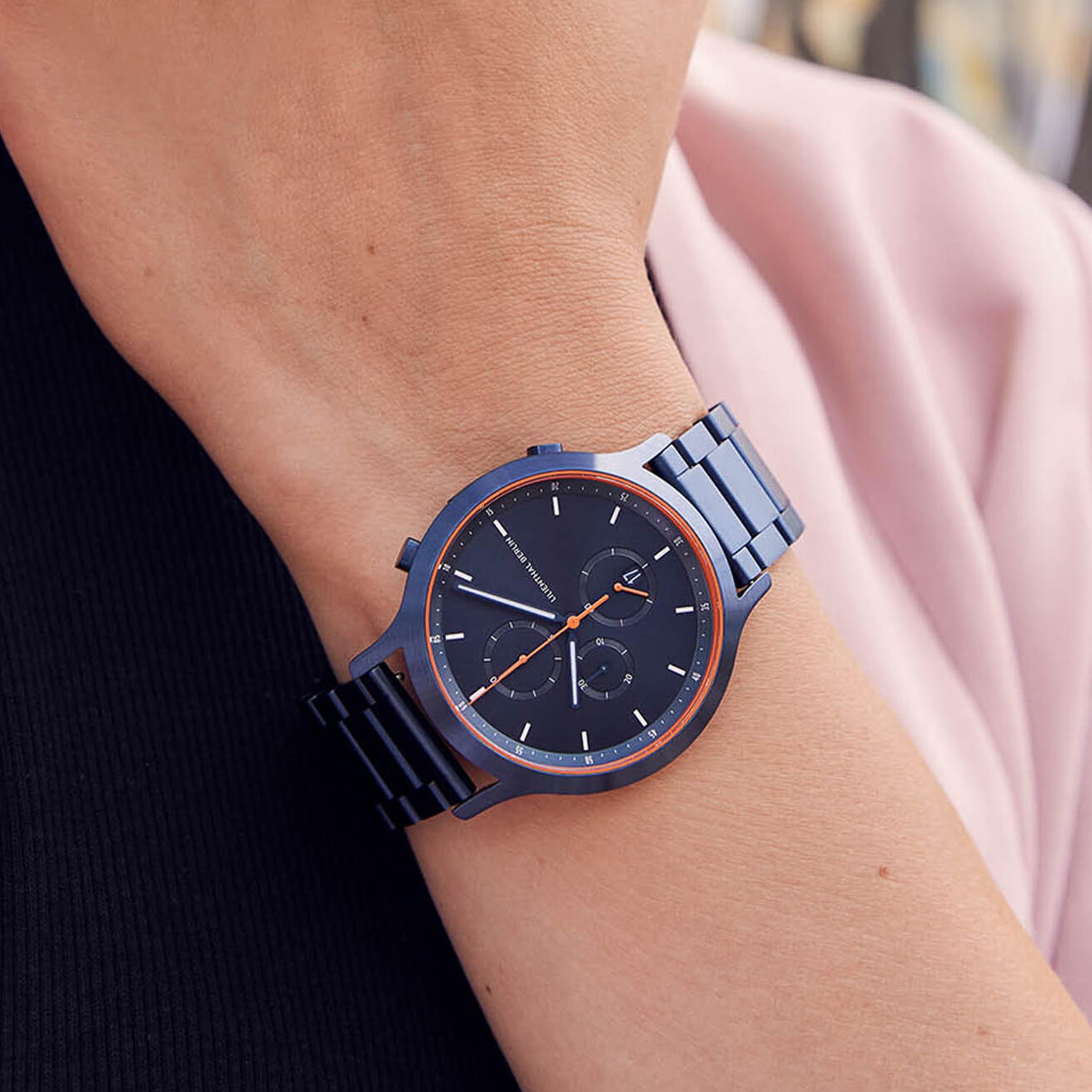 Sleek blue metal chronograph watch with orange accents on wrist, modern minimalist design