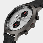 Minimalist chronograph watch with black leather strap, silver dial, and red-accented subdials