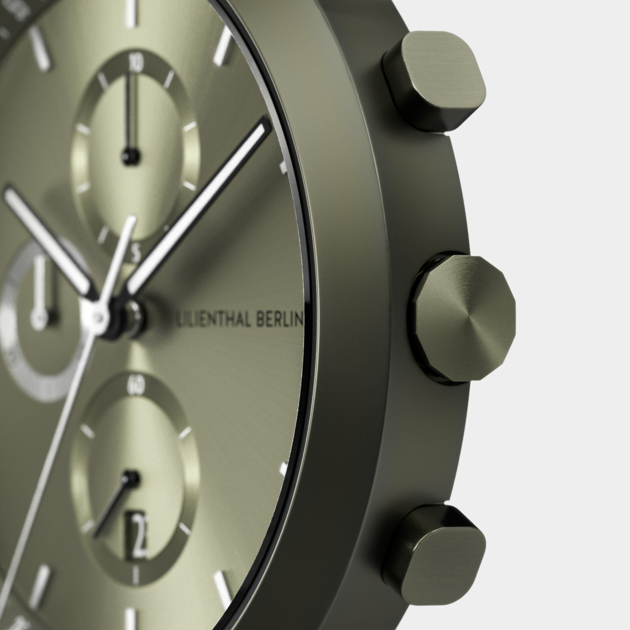 Close-up of a modern chronograph watch face with subdials, matte olive green finish, and side buttons.