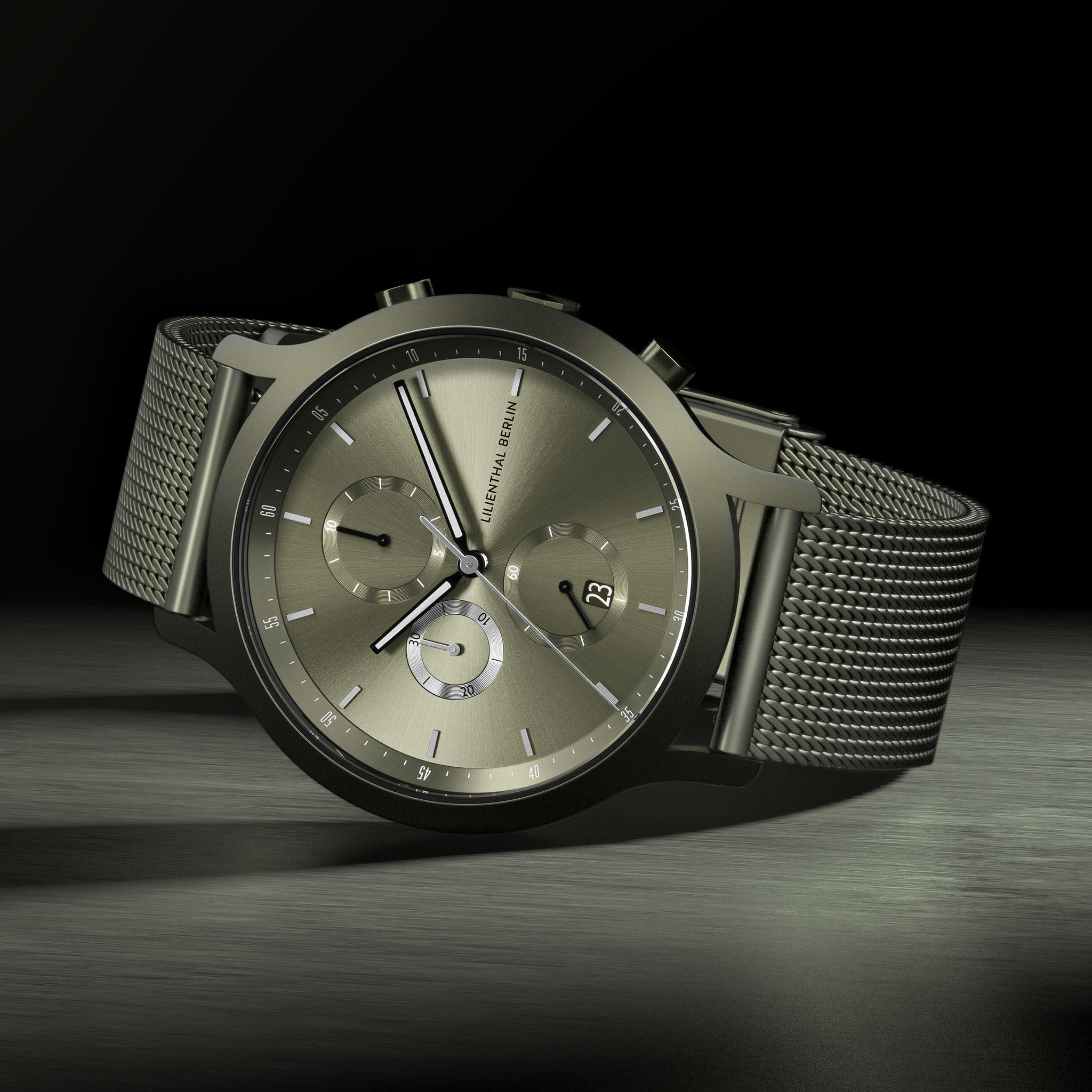 Minimalist mesh band chronograph watch with metallic dial and date display on dark background