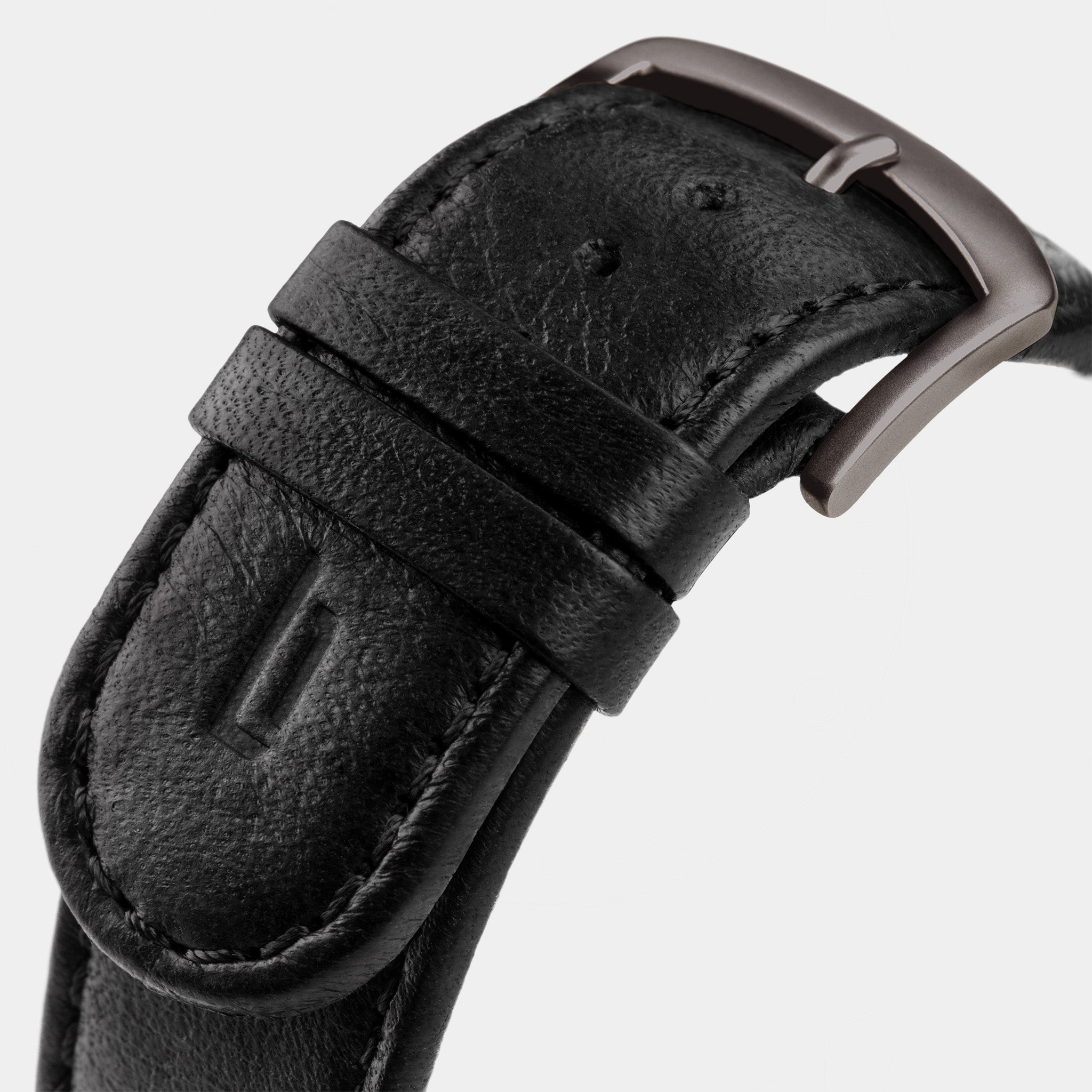 Close-up of black leather watch strap with silver buckle on light background