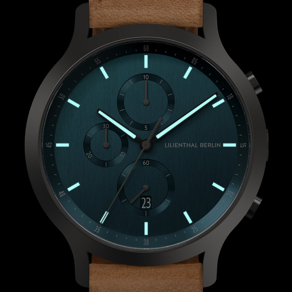 Minimalist black and teal chronograph watch with luminous hands and brown leather strap