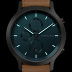 Minimalist black and teal chronograph watch with luminous hands and brown leather strap