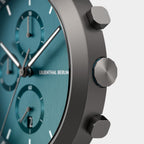 Close-up of a modern teal chronograph watch face with metallic case and push buttons