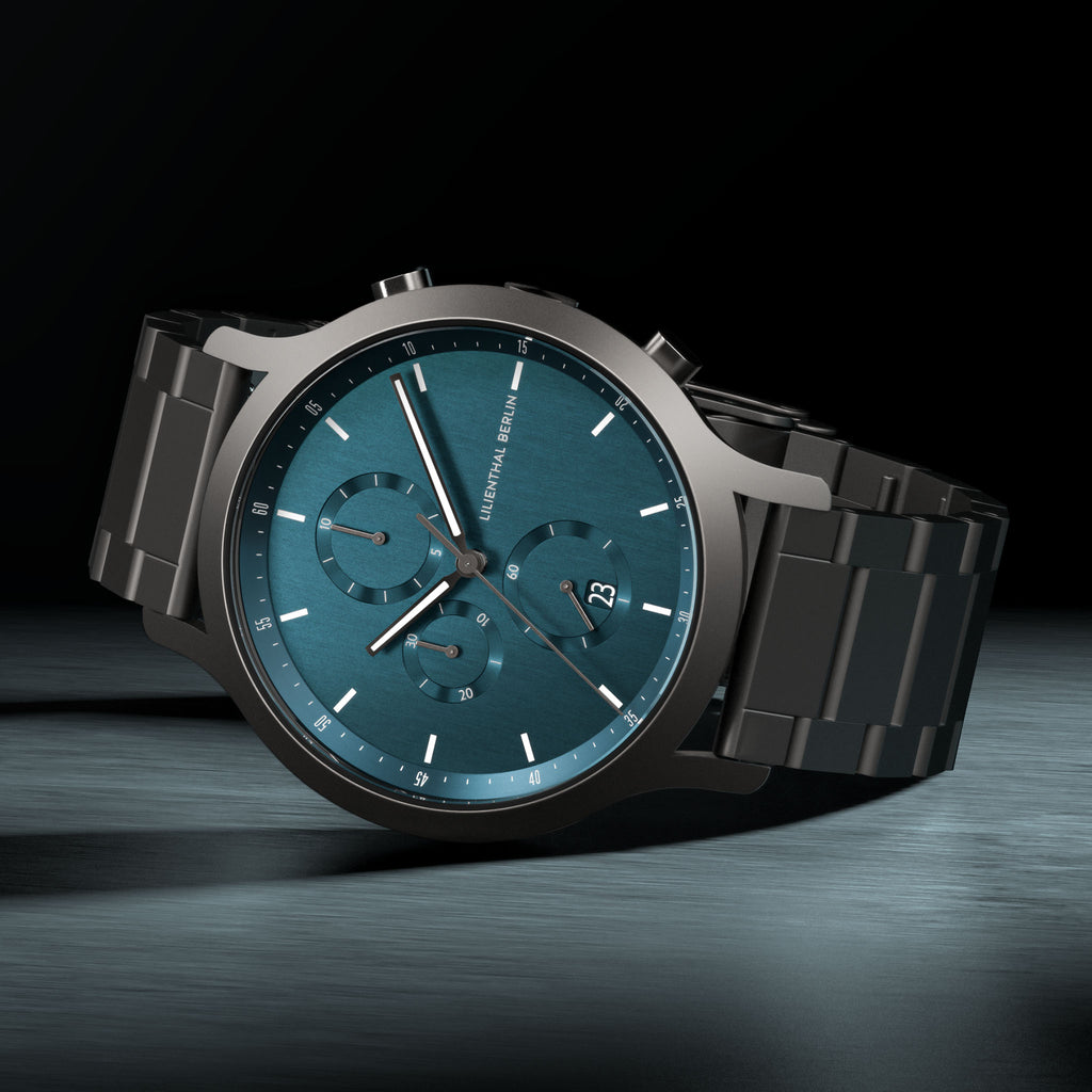 Men's chronograph watch with teal dial, date display, and black metal strap on dark background