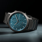 Men's chronograph watch with teal dial, date display, and black metal strap on dark background