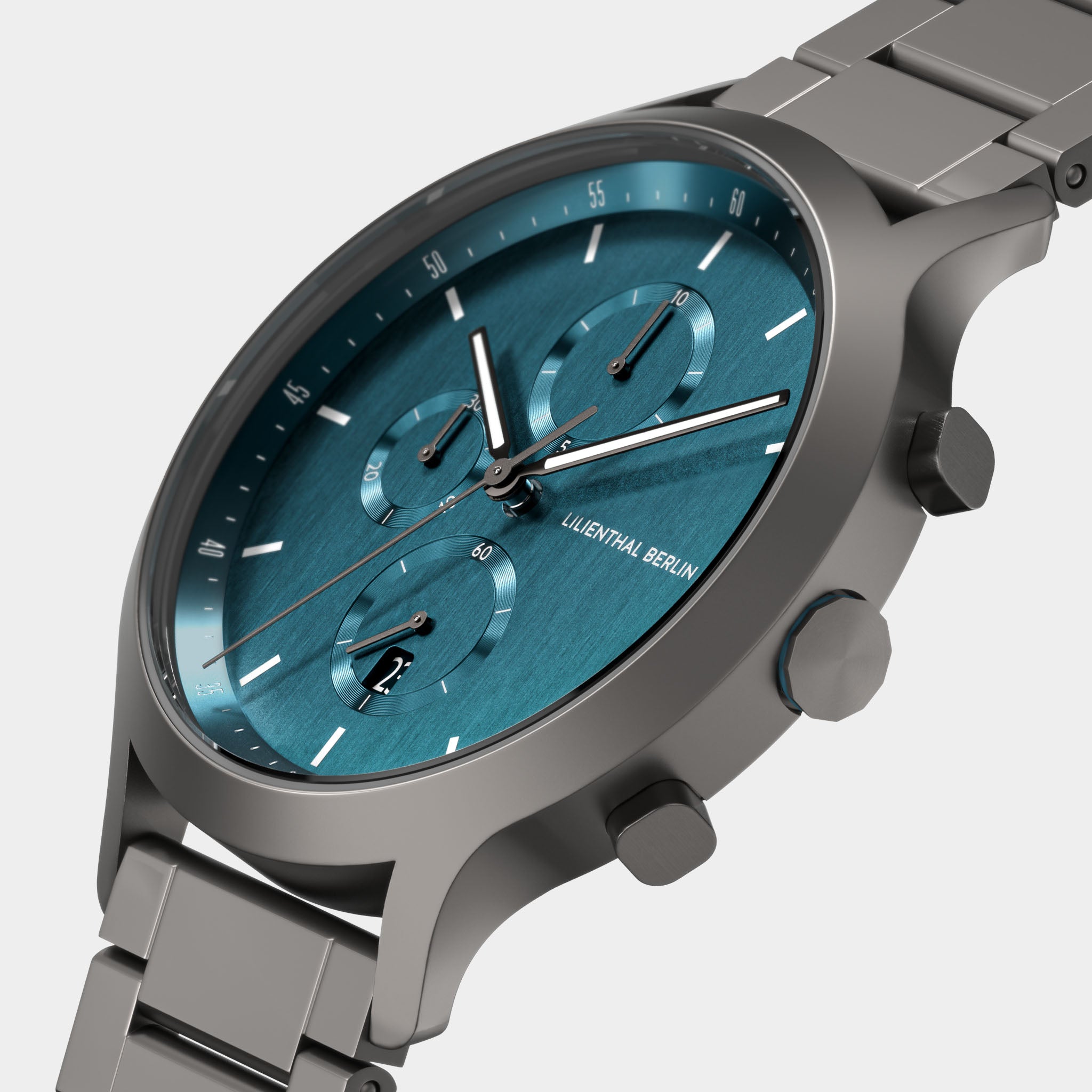 Close-up of a modern chronograph watch with a teal dial, stainless steel strap, and subdials.