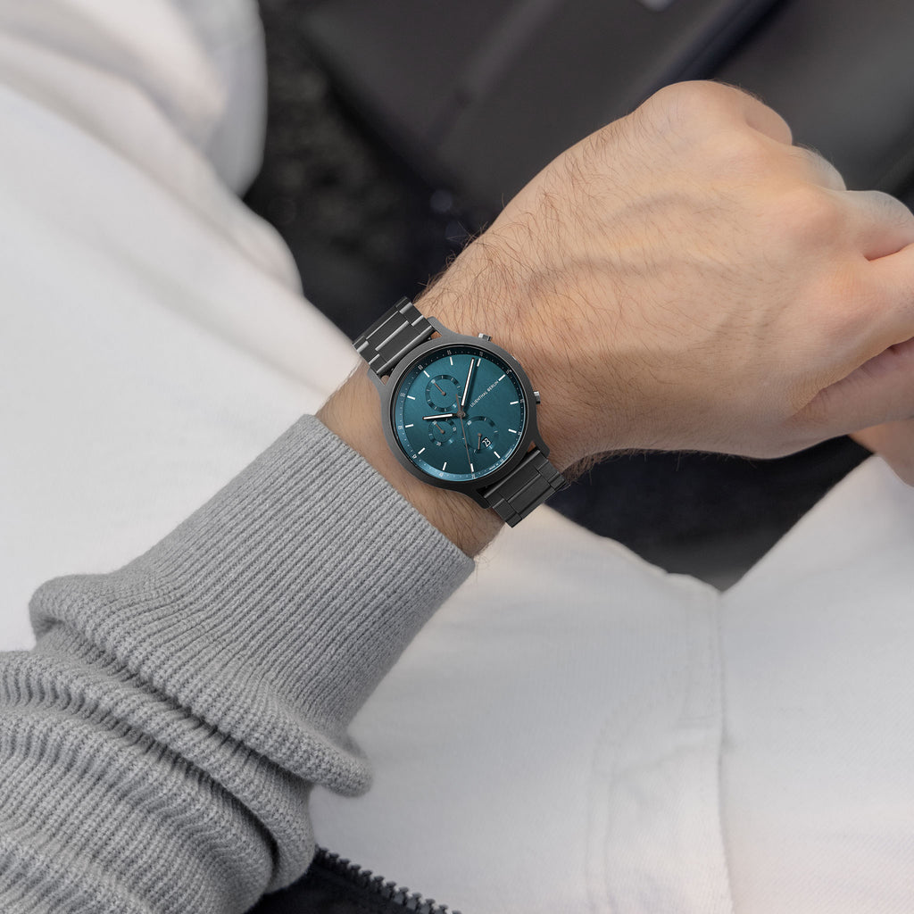 Man wearing a modern teal dial stainless steel wristwatch with chronograph design