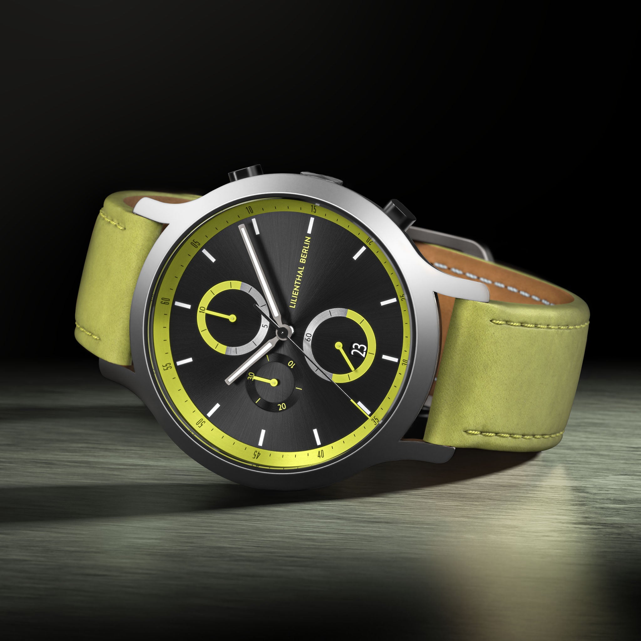 Chronograph watch with black dial, yellow accents, and green leather strap on metallic surface