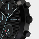 Close-up of a black chronograph watch with textured dial, subdials, and solar indicator