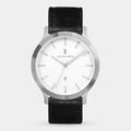 Minimalist silver wristwatch with a white dial, black leather strap, and date display.