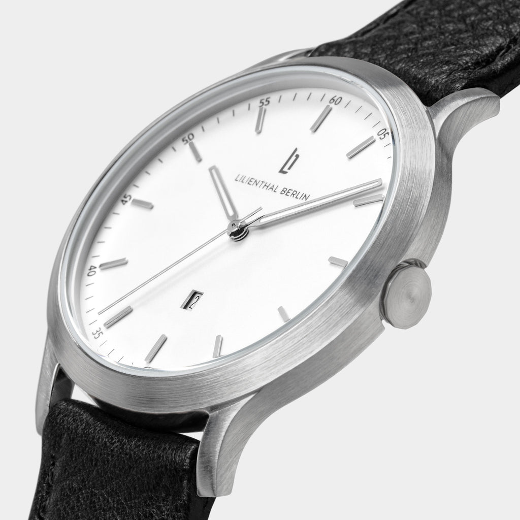 Minimalist silver wristwatch with white dial, black leather strap, and date display