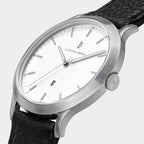 Minimalist silver wristwatch with white dial, black leather strap, and date display