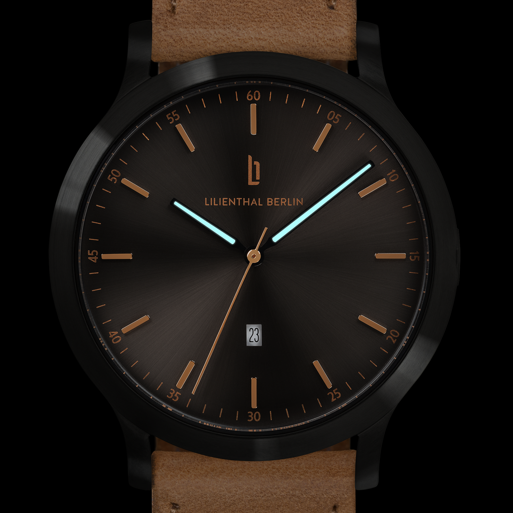Modern black watch with brown leather strap, minimalist dial, gold accents, and date display