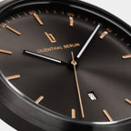 Close-up of minimalist black watch face with gold markers, sleek hands, and date display.