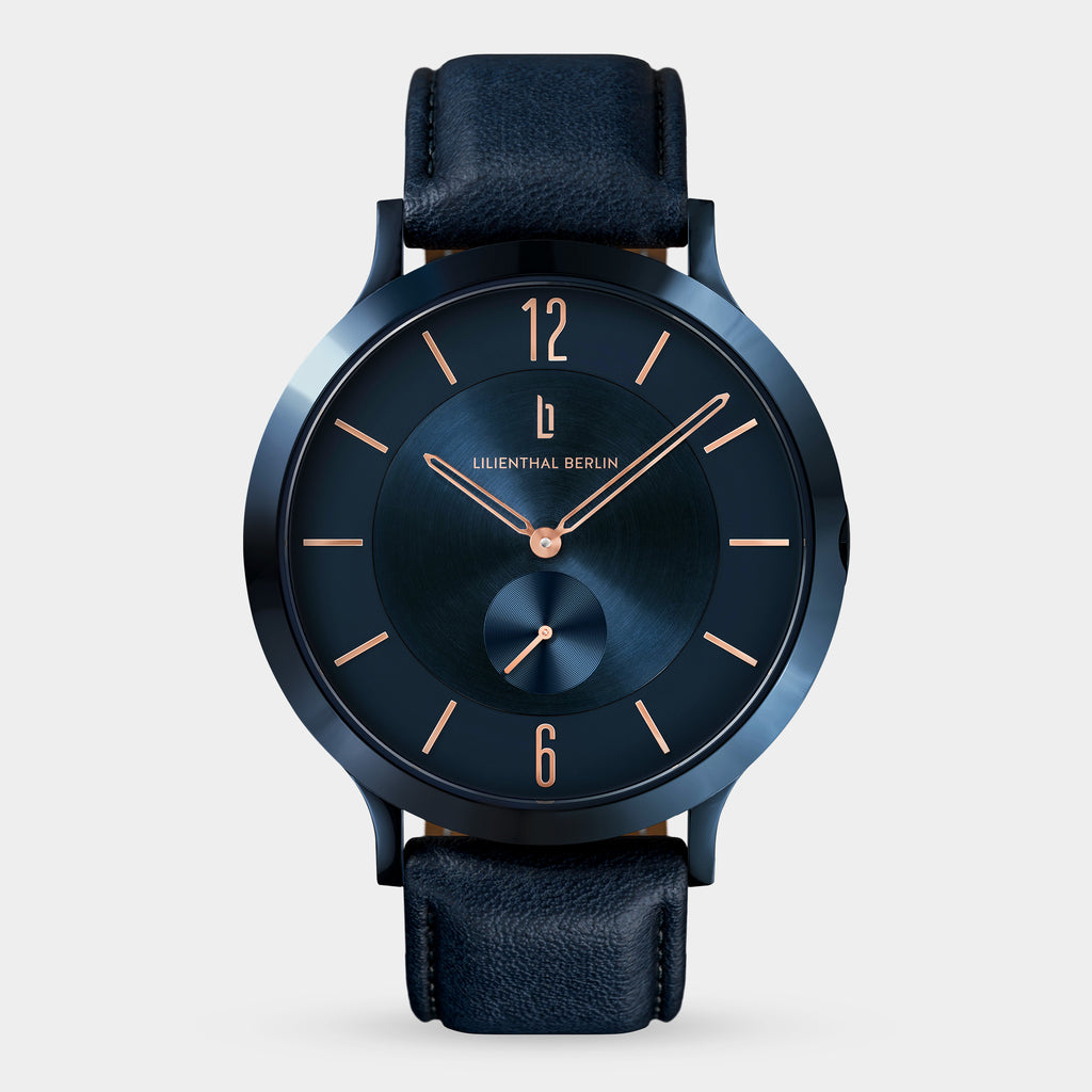 Elegant blue minimalist watch with rose gold hands and black leather strap on white background