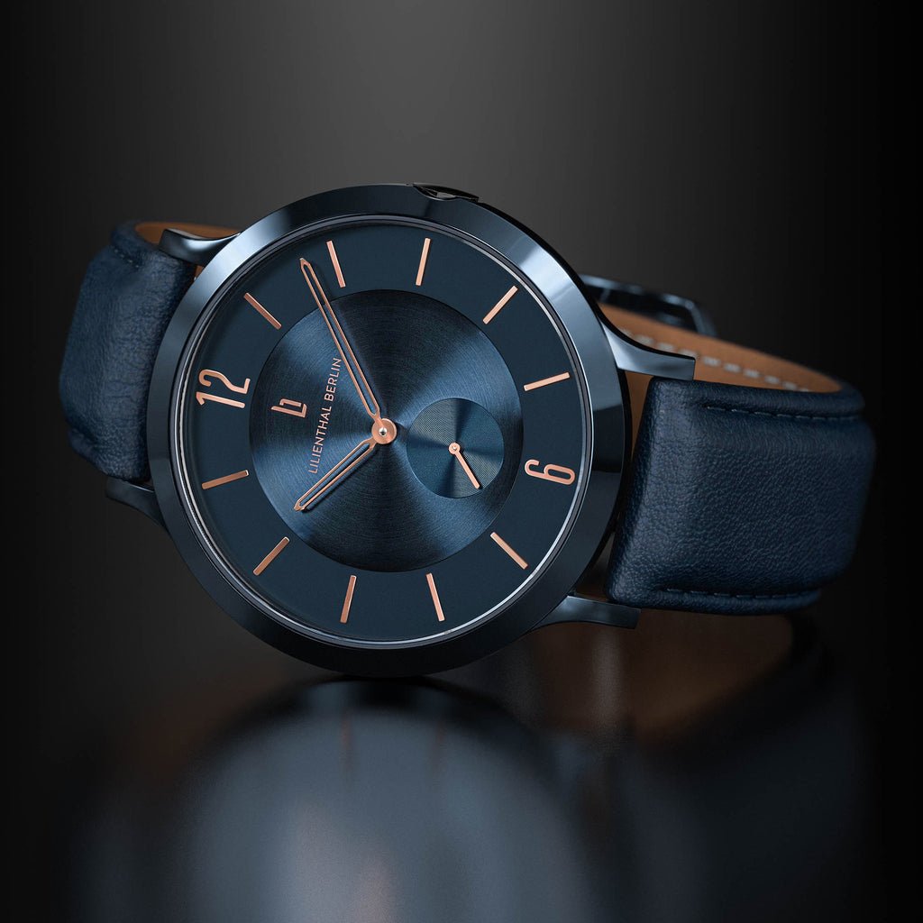 Elegant black wristwatch with rose gold markers and dark leather strap on a reflective surface